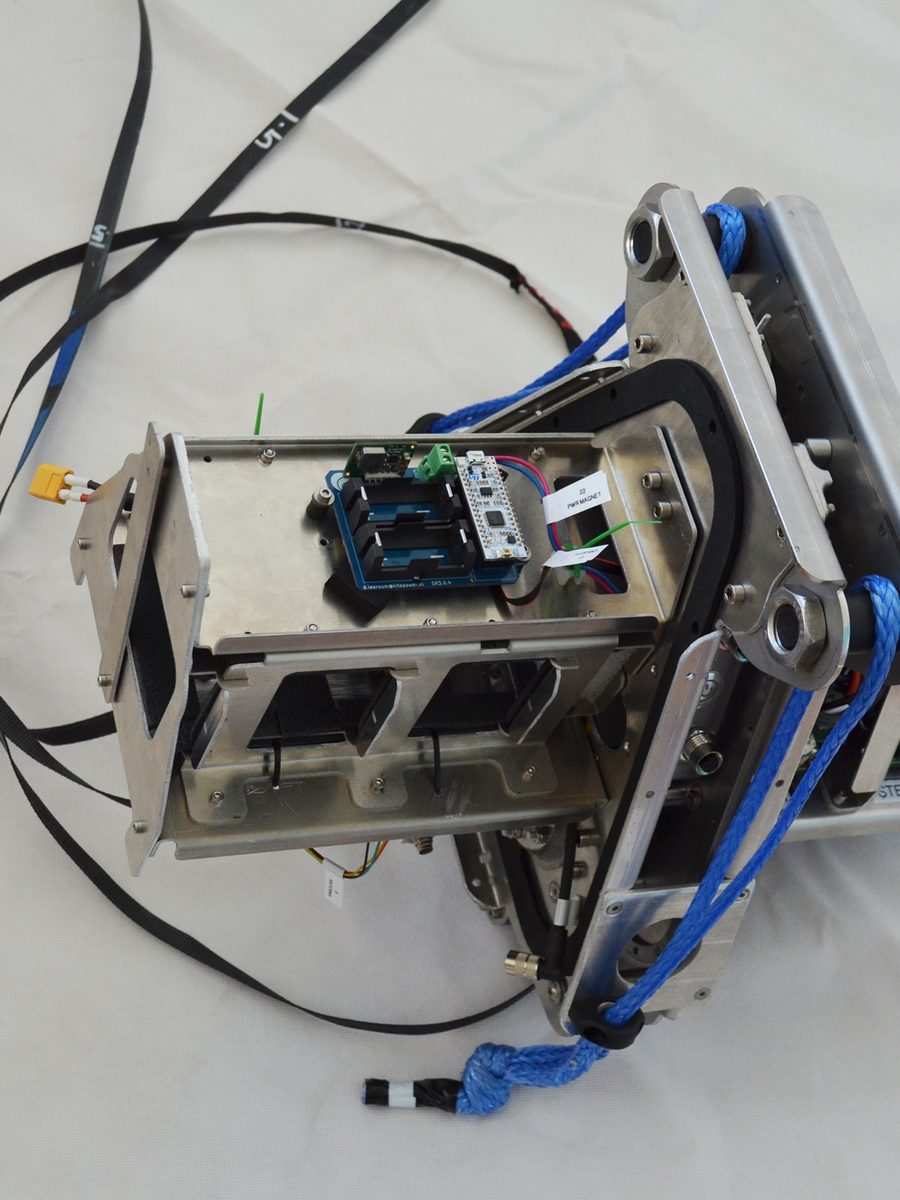 A machined aluminium actuator assembly on the bench, with control boards and a cable harness built into the frame