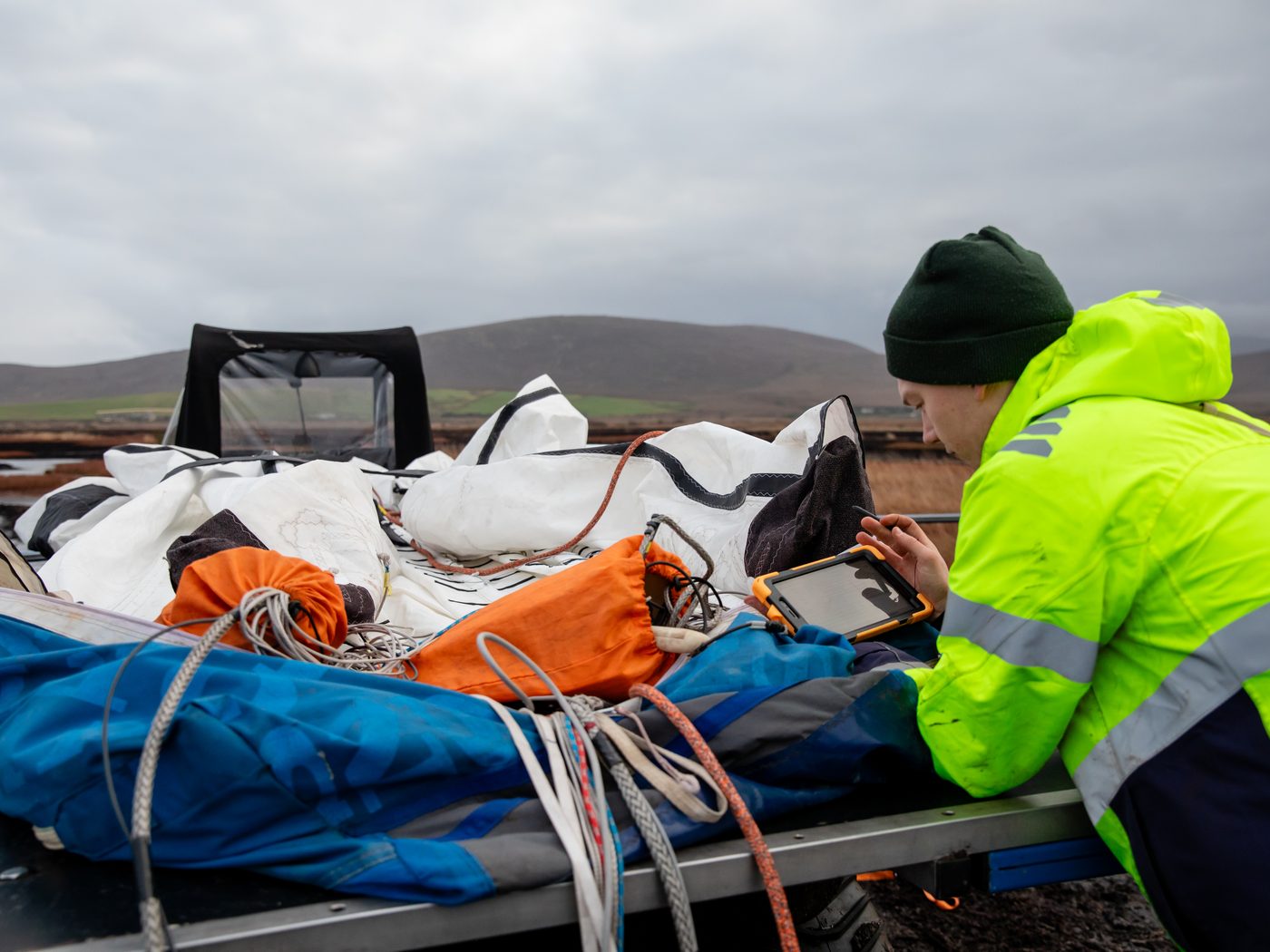 An engineer in a high-visibility jacket using a rugged tablet beside a packed wing laid out on a trailer