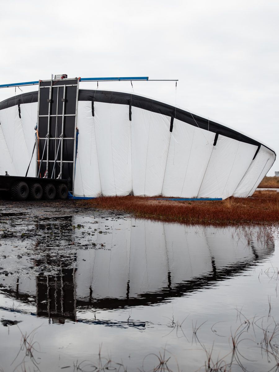 An inflated wing standing on its launch trolley in a flooded peat field, mirrored in the water below