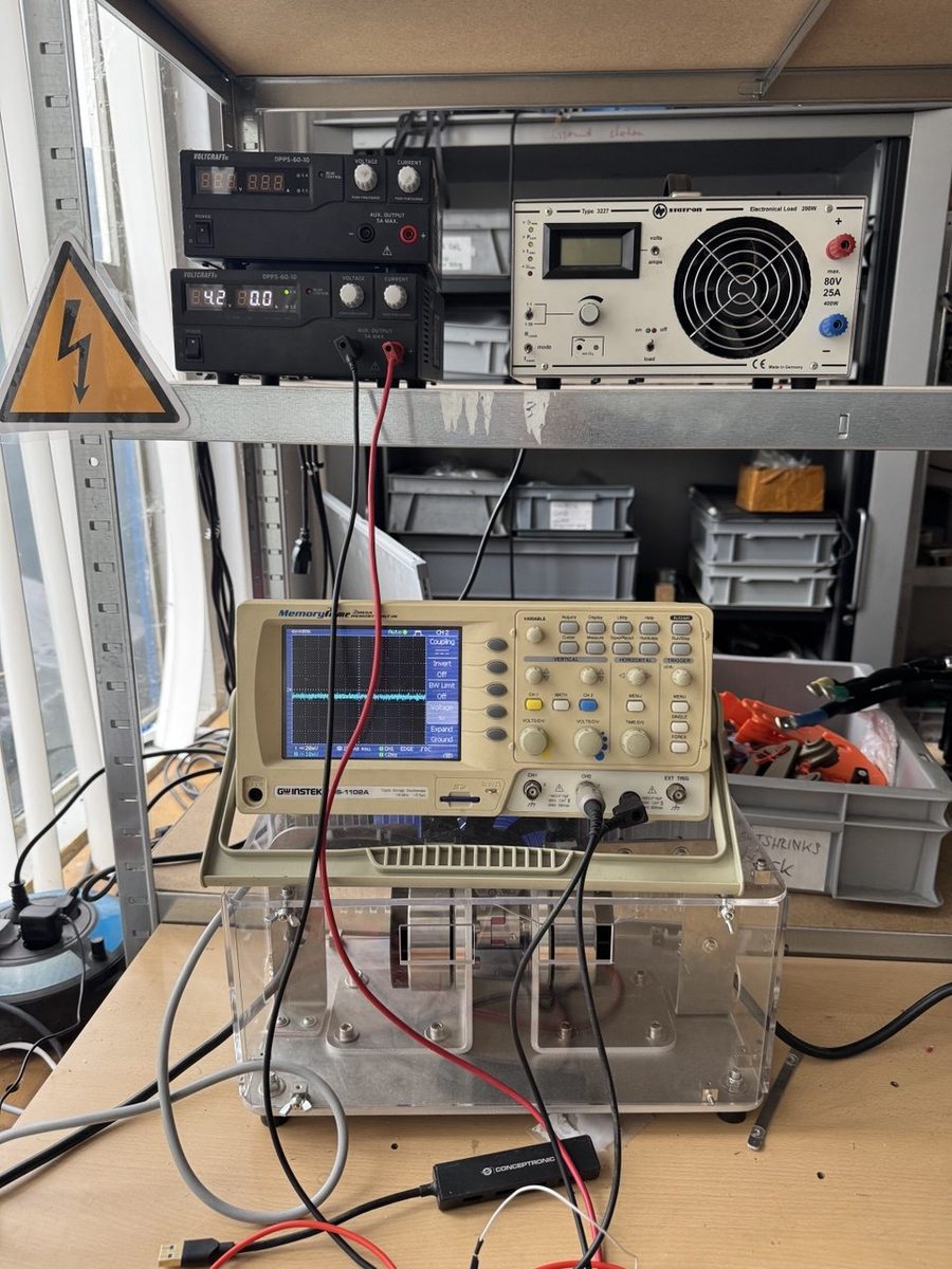 A bench with an oscilloscope, a bench power supply and a board under test in an acrylic fixture