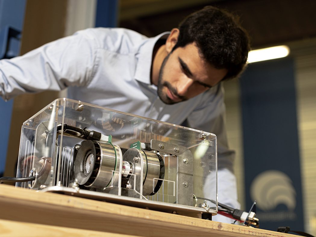 An engineer leaning over a rotor and clutch assembly in a clear-walled test case on a workbench